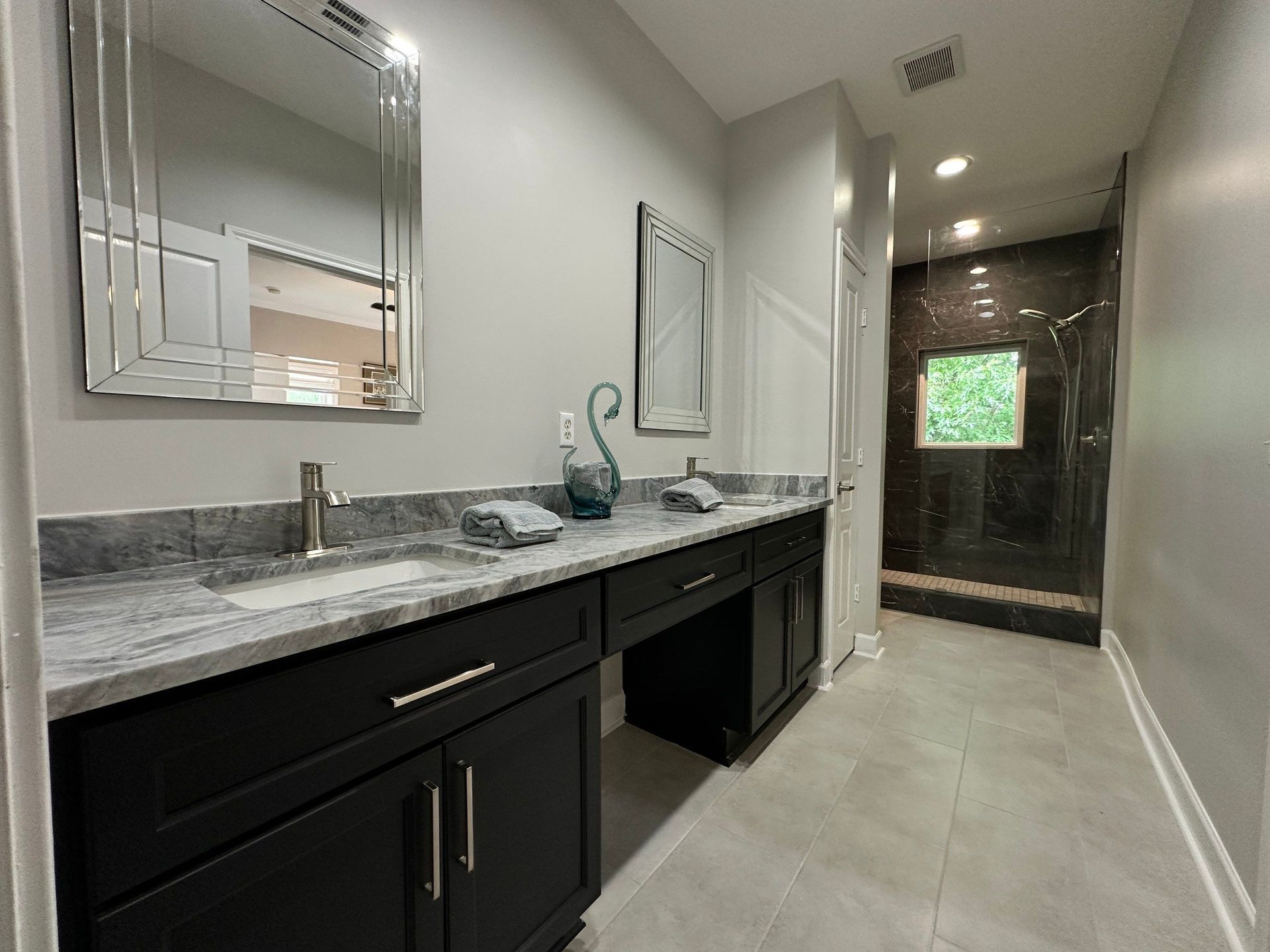 Long, narrow bathroom vanity with dark cabinets, gray stone countertop, and walk-in shower at the end.