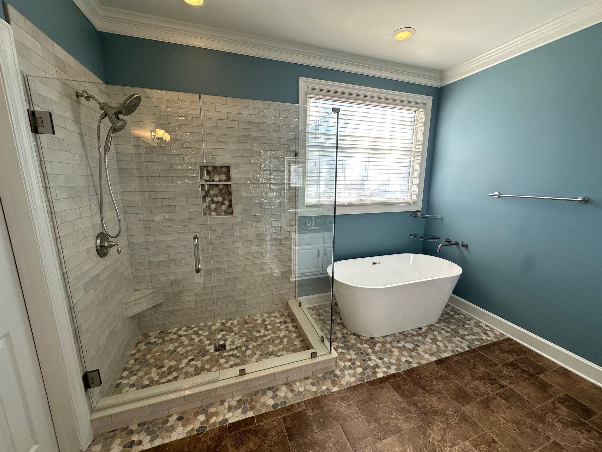 Modern bathroom with tiled walk-in shower, freestanding tub, blue walls, and window blinds