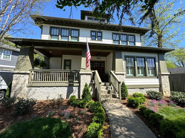 Historic house with front porch, stairs, and an American flag amid garden landscaping