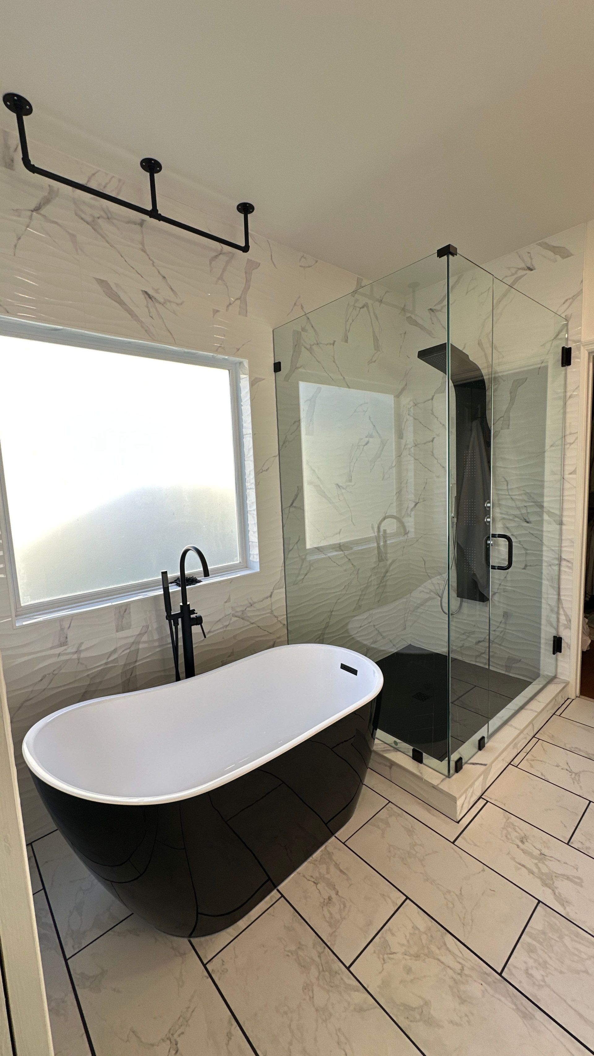 Modern bathroom with freestanding tub, glass shower, large window, and light tile flooring