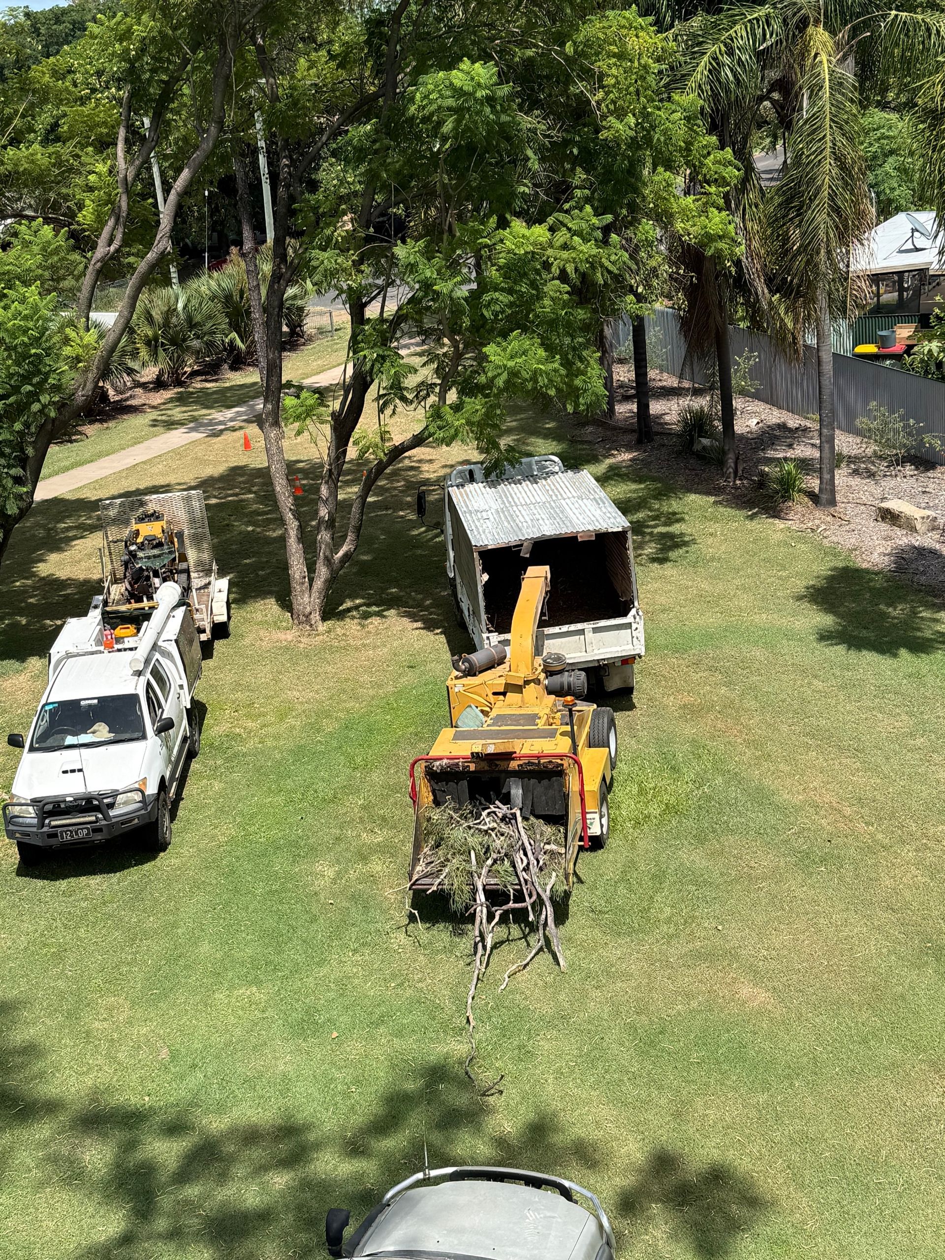 A white utility truck and a wood chipper parked on a grassy field with a large dump truck in the background.