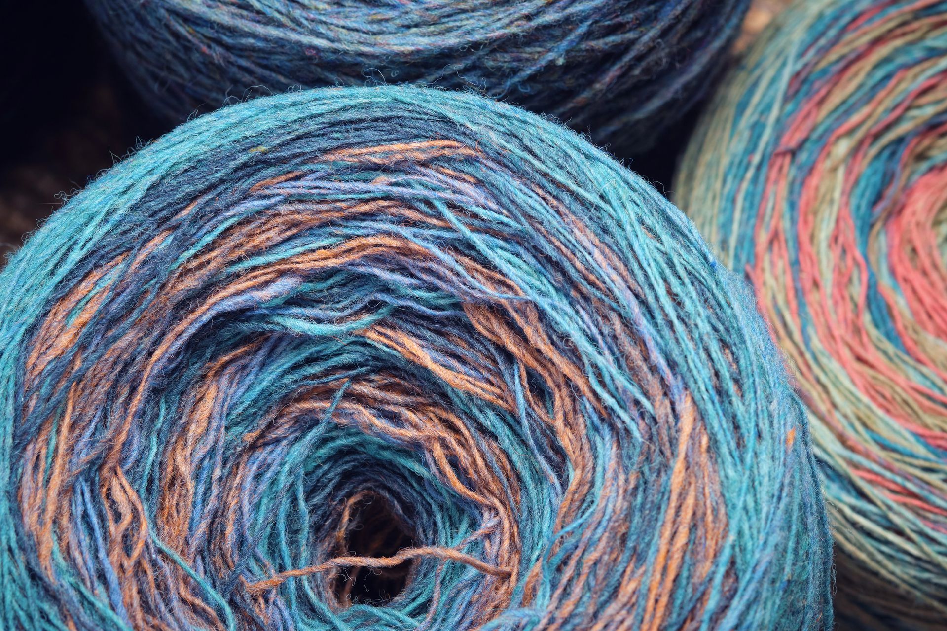 Primo piano di tre gomitoli di filato variegato nelle tonalità del blu, verde acqua e arancione.