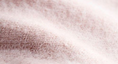 Primo piano di un soffice tessuto rosa chiaro dalla consistenza leggermente increspata.