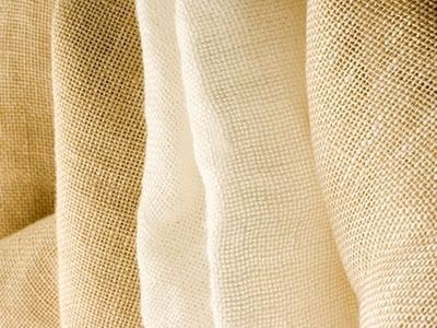 Primo piano di tessuto di iuta beige in diverse tonalità, che ne evidenzia la consistenza e le pieghe.