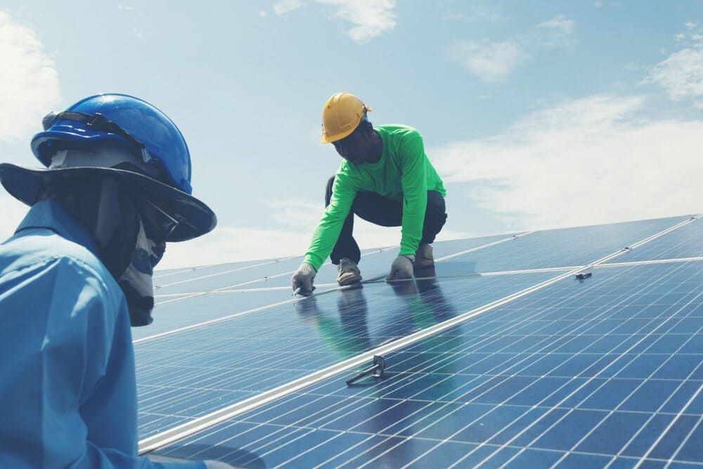 Two Men Are Working On A Solar Panel On Top Of A Building — Solarblu Pty Ltd In Woonona, NSW