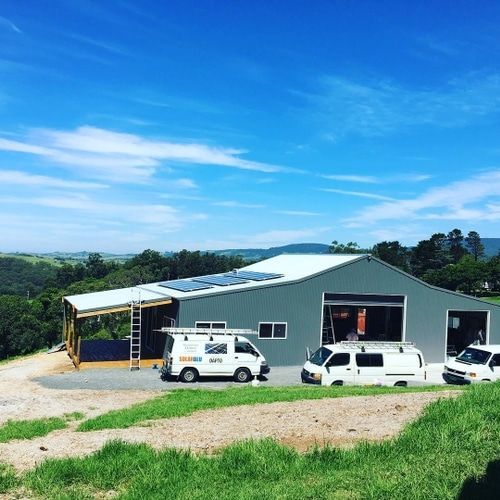 Two Vans Are Parked in Front of a Building With Solar Panels on the Roof — Solarblu Pty Ltd in Kangaroo Valley, NSW