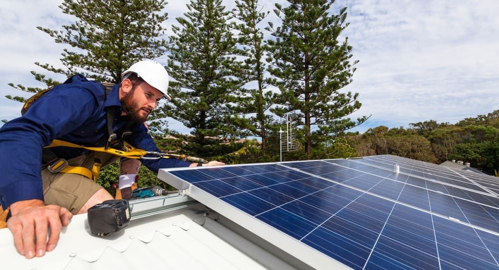 A Man Is Installing Solar Panels On A Roof — Solarblu Pty Ltd In Kiama, NSW
