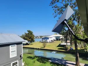Canal-side houses and trees under a bright blue sky, with a solar panel in the foreground