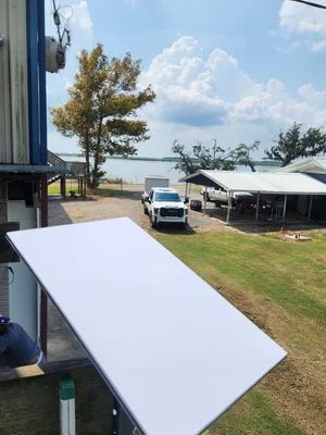 A white board on a balcony overlooks a grassy yard with a parked truck, shelter, and ocean beyond.
