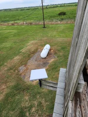 White propane tank near a wooden deck on a grassy yard with open fields in the background