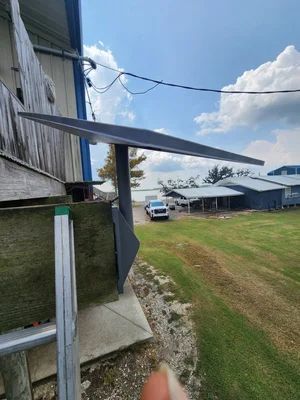 Side view of a metal building with a long roof overhang, grassy yard, white van, and cloudy sky