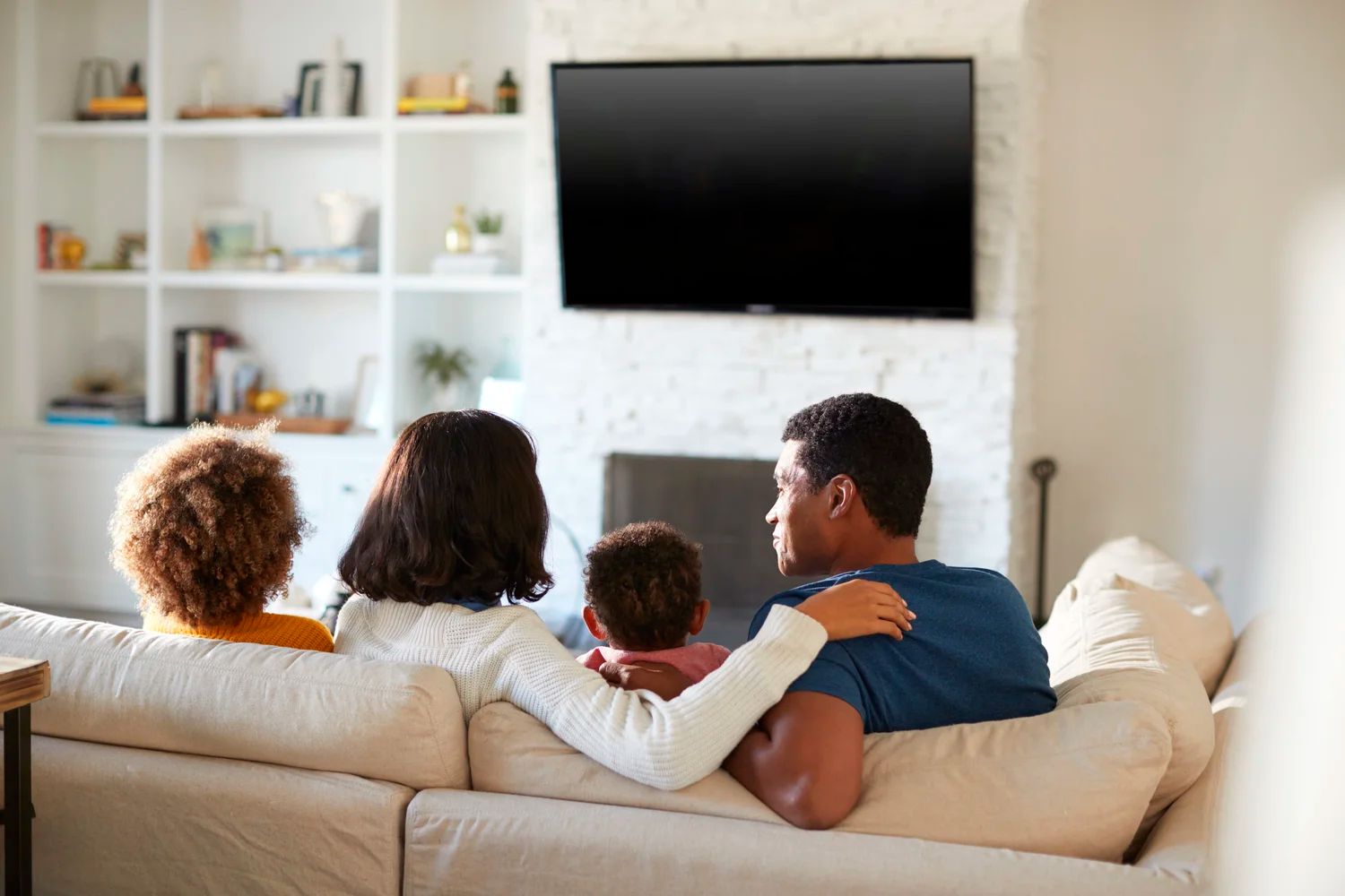Family sitting on a couch watching TV in a bright living room