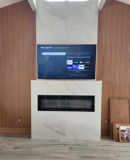 Modern fireplace wall with wood slats, white marble surround, and a mounted TV displaying a streaming menu.