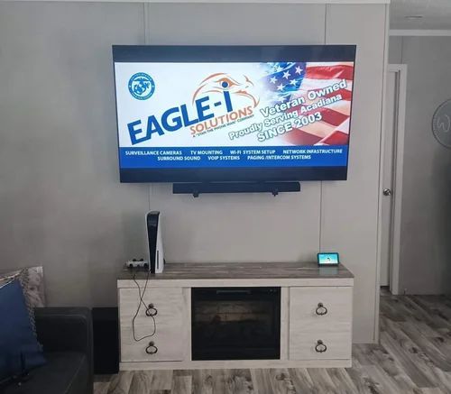 Wall-mounted TV showing Eagle-I Solutions logo above a white console with a gaming console in a living room