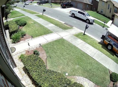 Sunny suburban street with sidewalks, lawns, parked white van, and a person walking on the sidewalk