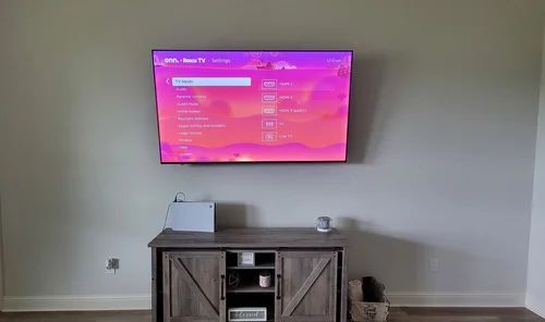 Wall-mounted TV with a pink screen above a wooden media cabinet in an empty room.