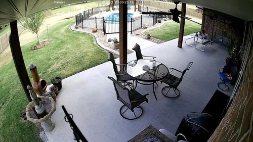 Covered backyard patio with metal table and chairs, a dog near the steps, and a pool in the background