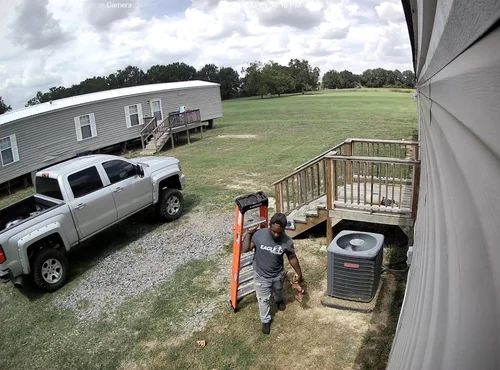 Person walking beside a white pickup truck near a house and wooden deck in a grassy yard.