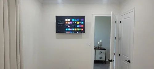 White hallway with a wall-mounted TV, open doorway, and a small cabinet in the adjacent room