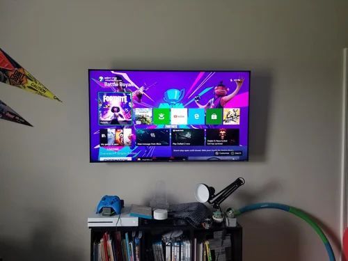 Wall-mounted TV showing a purple game console home screen above a cluttered shelf with toys and cables