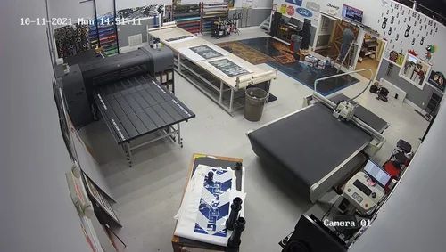 Empty workshop with tables, equipment, and posters, viewed from a security camera angle