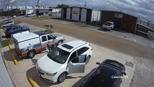 Parking lot with white SUV and trucks; one vehicle door is open near a warehouse building.