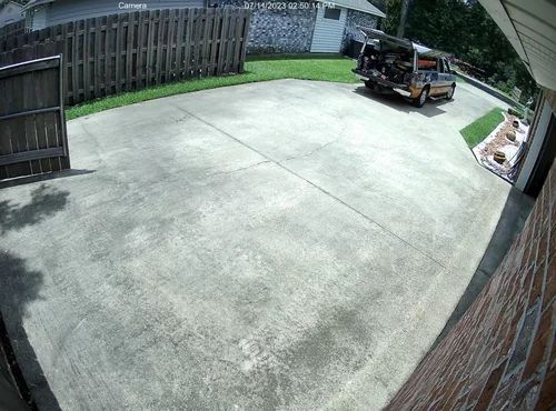 Empty concrete driveway beside a wooden fence, with a parked utility cart near the back fence.
