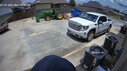 Driveway with a silver pickup truck, green tractor, and trash bins in a suburban home driveway.