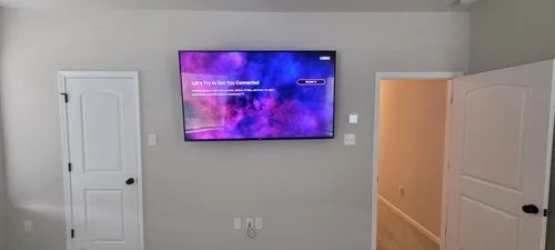 Living room wall with a mounted TV, two white doors, and an open doorway to a lit hallway.