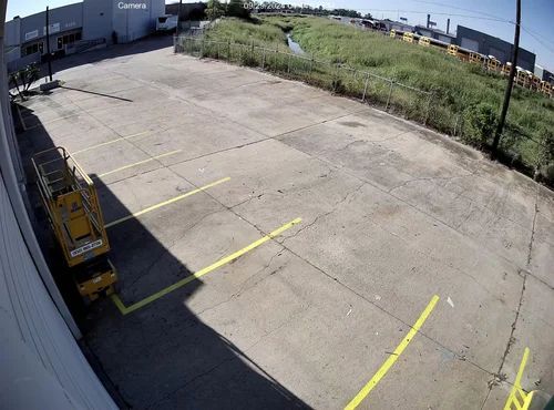 Empty concrete parking lot with yellow lines beside a warehouse and grassy field under bright sun