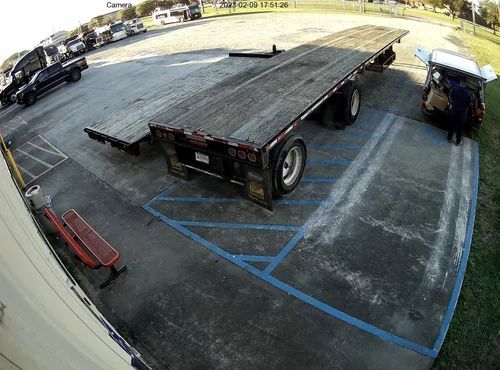 Flatbed trailer in a parking lot with a forklift beside it and a red bench in the foreground