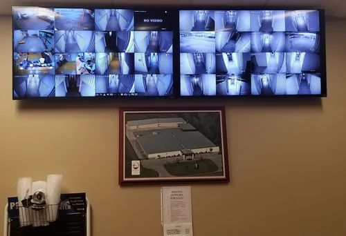 Security monitor wall showing multiple surveillance camera views above a framed building photo.