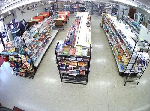 Overhead view of a brightly lit convenience store aisle with shelves of snacks and drinks.