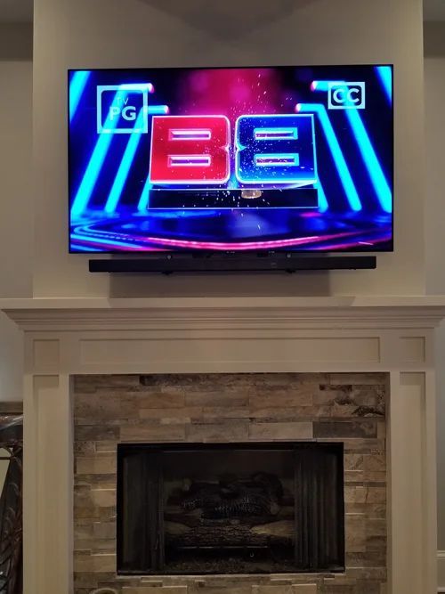TV above fireplace showing a neon game show graphic in a living room