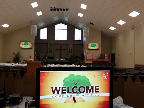 Church sanctuary with a welcome sign on a screen, rows of chairs, and a stage at the front