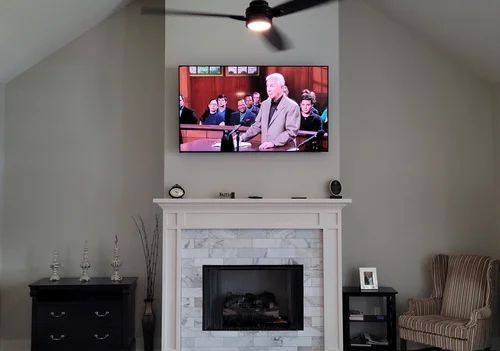 Living room with a TV above a white fireplace mantel, flanked by a cabinet and striped chair.