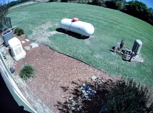 Backyard with a white propane tank, patio furniture, and lawn in bright daylight