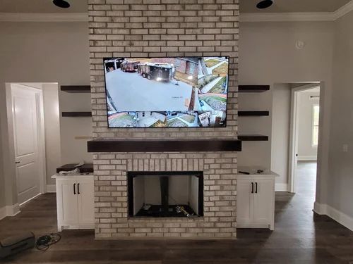 Living room with white brick fireplace and mounted TV displaying a security camera view