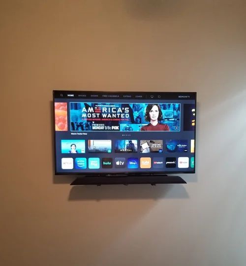 Wall-mounted TV displaying a streaming home screen in a beige room