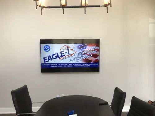 Conference room with wall-mounted TV displaying an Eagle One ad, black chairs, and a table under a ceiling light.