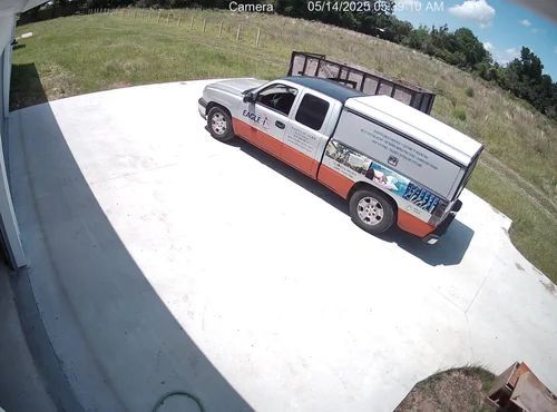 White pickup truck with utility bed parked on a concrete driveway beside a grassy field, viewed from above.
