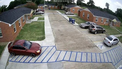 Parking lot with several cars and brick apartment buildings on both sides.
