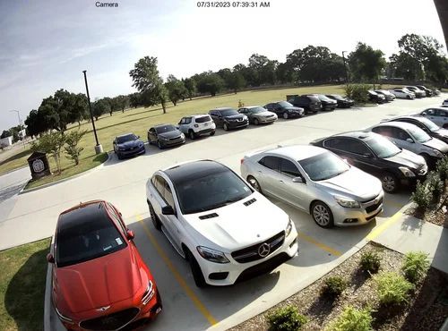 Parking lot with several parked cars, including a red car and white SUV in the foreground.