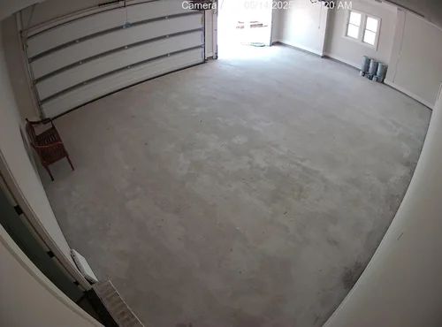 Empty garage interior with concrete floor, white walls, and bright light from an open door at the back.