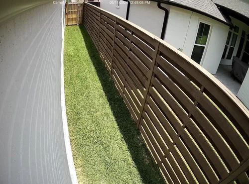 Narrow grassy side yard between white and brown houses with a wooden fence and walkway