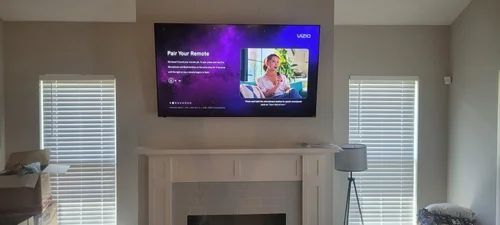 Living room with a wall-mounted TV above a fireplace, showing a purple streaming screen between two windows.