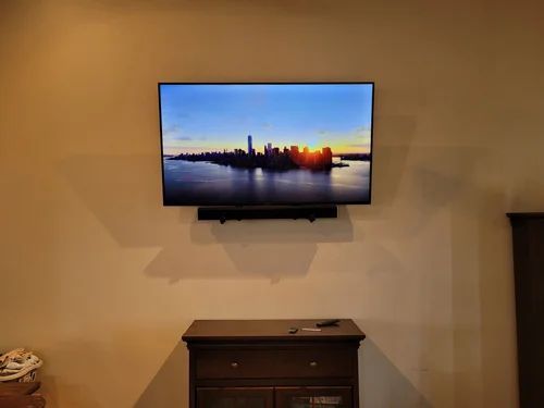 Wall-mounted TV showing a sunset skyline above a dark dresser in a beige room