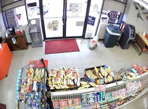 Convenience store checkout area with candy displays, red entrance mat, and front doors.