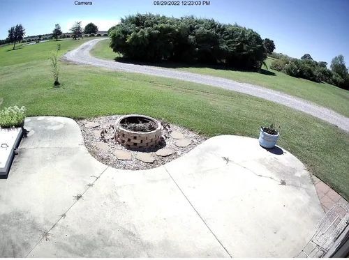 Patio overlooking a green lawn and curving driveway, with a stone fire pit and potted plant.