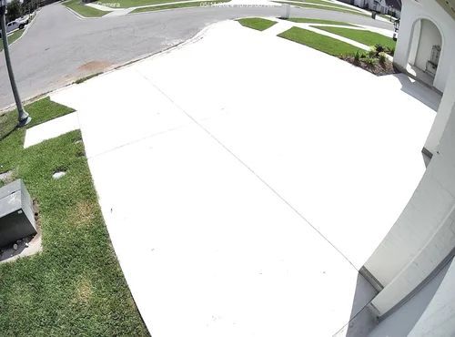 Bright suburban driveway and front yard with white concrete, grass, and a house entrance